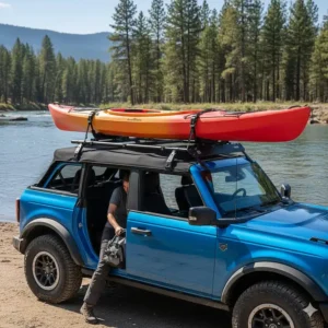 An action shot of a blue Bronco with the soft top down, fitted with a specialized roof rack and a kayak attachment ready for transport.